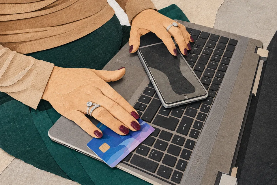 Člověk drží platební kartu a smartphone vedle notebooku.