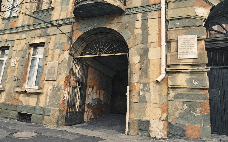 Ošlehaná kamenná fasáda v Sololaki s klenutým vstupem na dvůr a kovanou bránou.